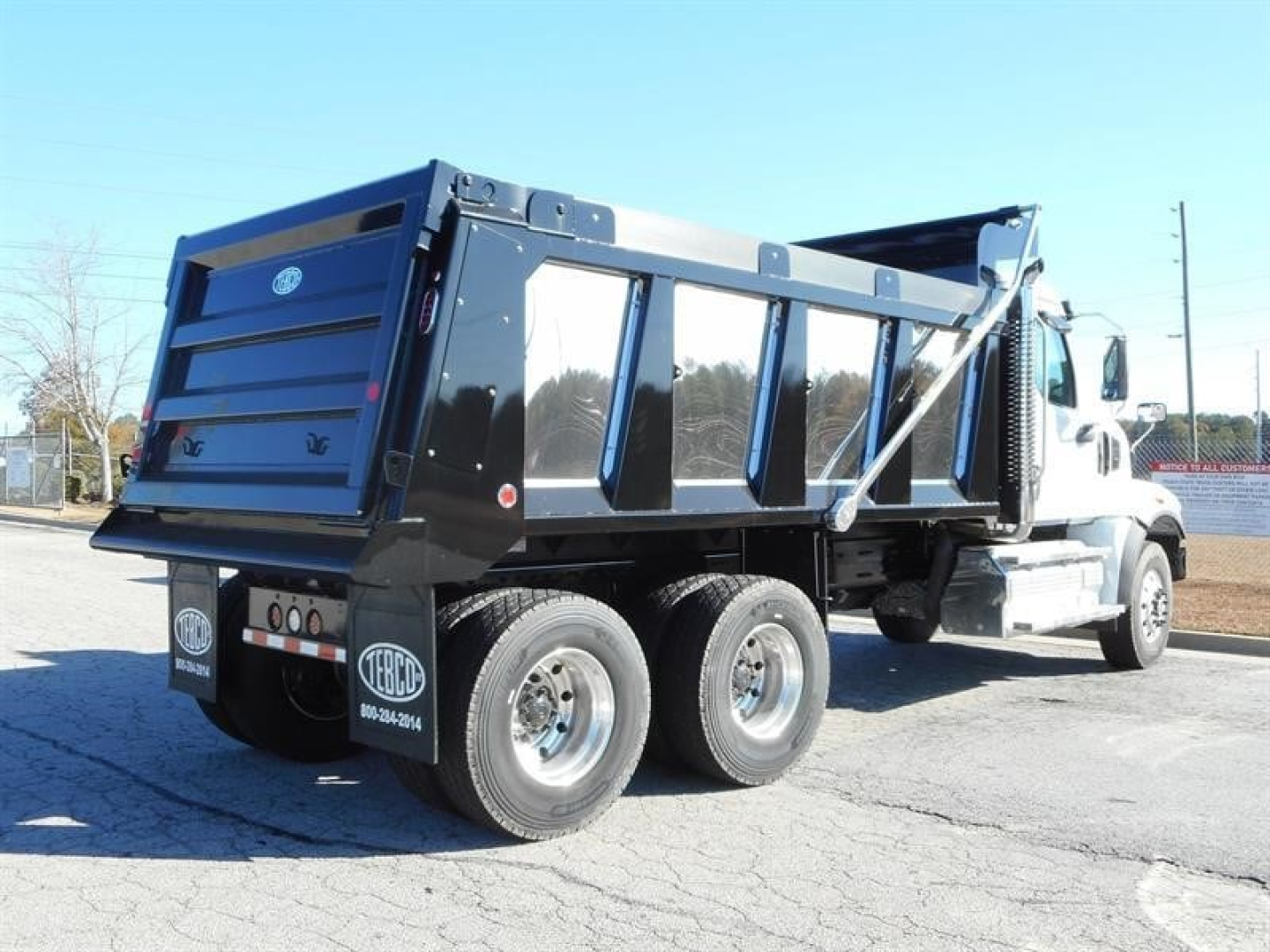 Dump truck rear three-quarter view showing cargo bed and dual rear axles with branding stickers on wheels.