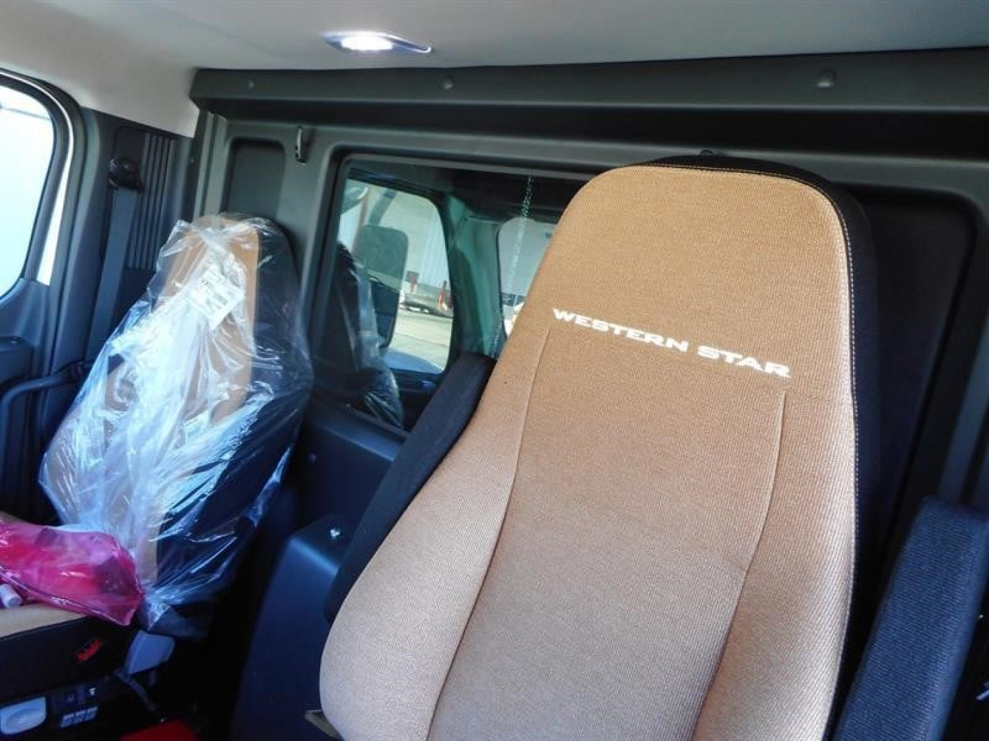 Western Star 47X truck interior with beige seat that has 'WESTERN STAR' embroidered, plastic-covered passenger seat, window, and cabin area visible.