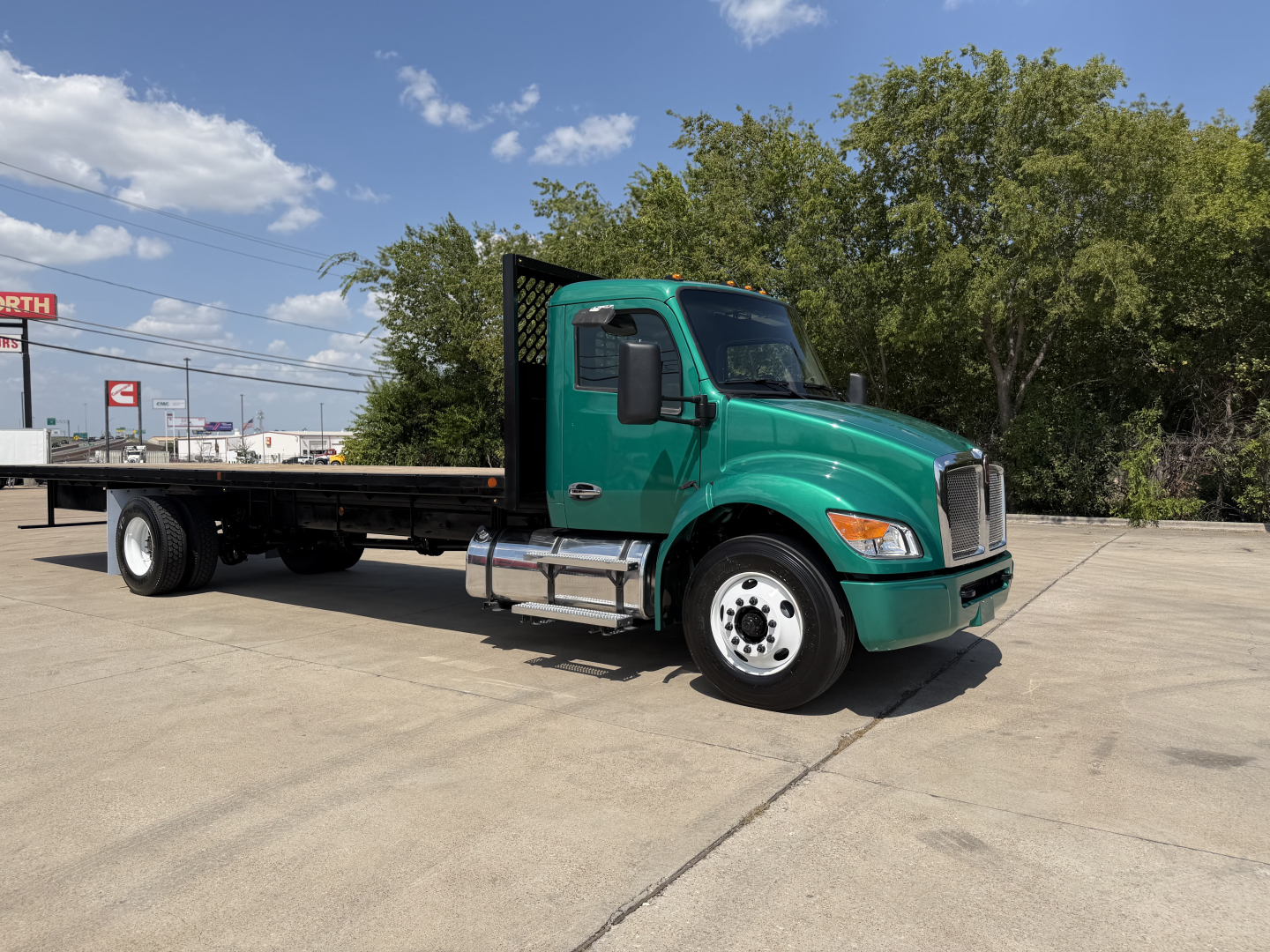 Green Kenworth T280 flatbed truck side view showing cab, flatbed, chassis, and rear wheels with clear sky.