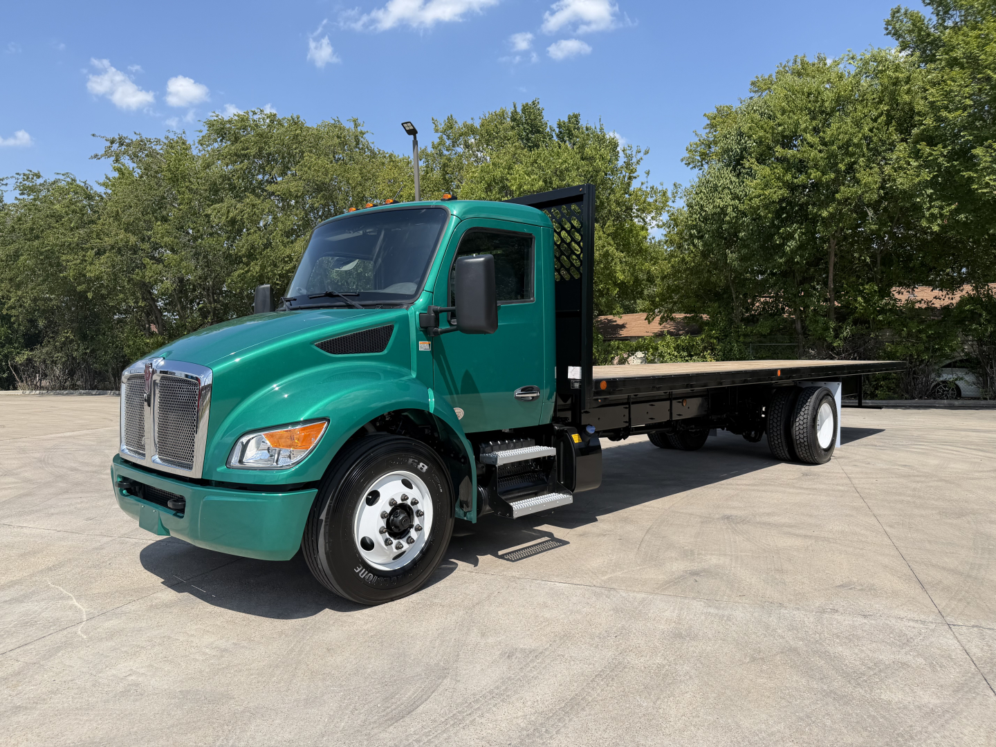 Kenworth T280 flatbed truck in green with a long black flatbed, front grille, and dual rear wheels in a paved lot.