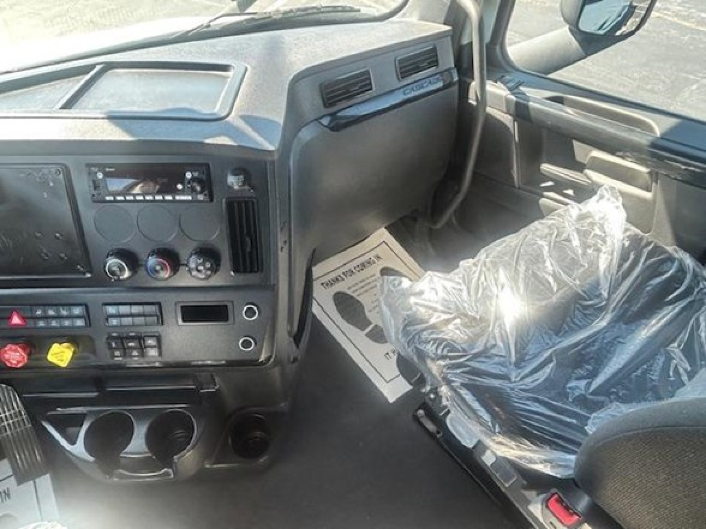 Interior of a Freightliner Cascadia 126 cab showing dashboard controls and steering area with plastic-covered seat.