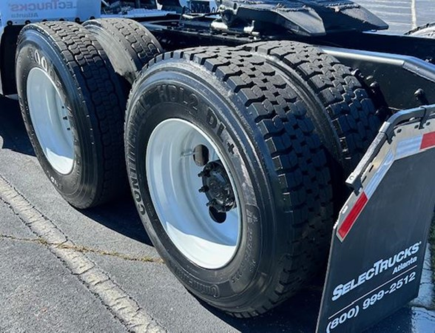 Triple axles truck rear wheels with heavy-duty tires and mud flaps showing Freightliner Cascadia 126 equipment labels.