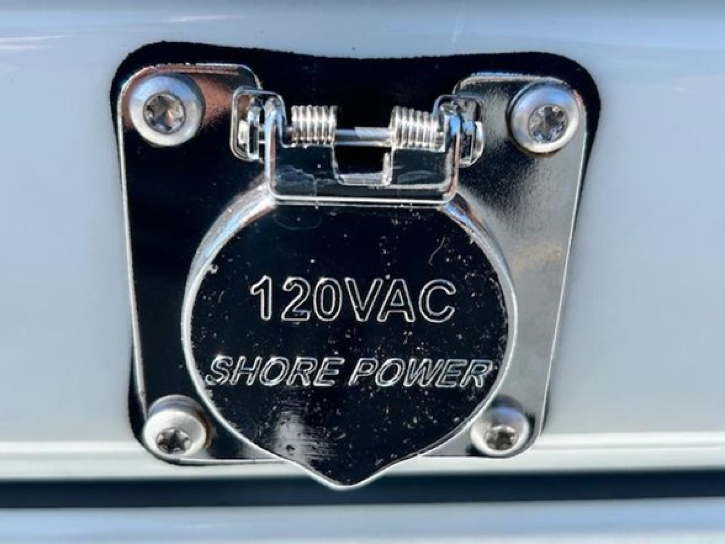 120V AC shore power inlet cover on Freightliner Cascadia 126, chrome with four screws and hinge.
