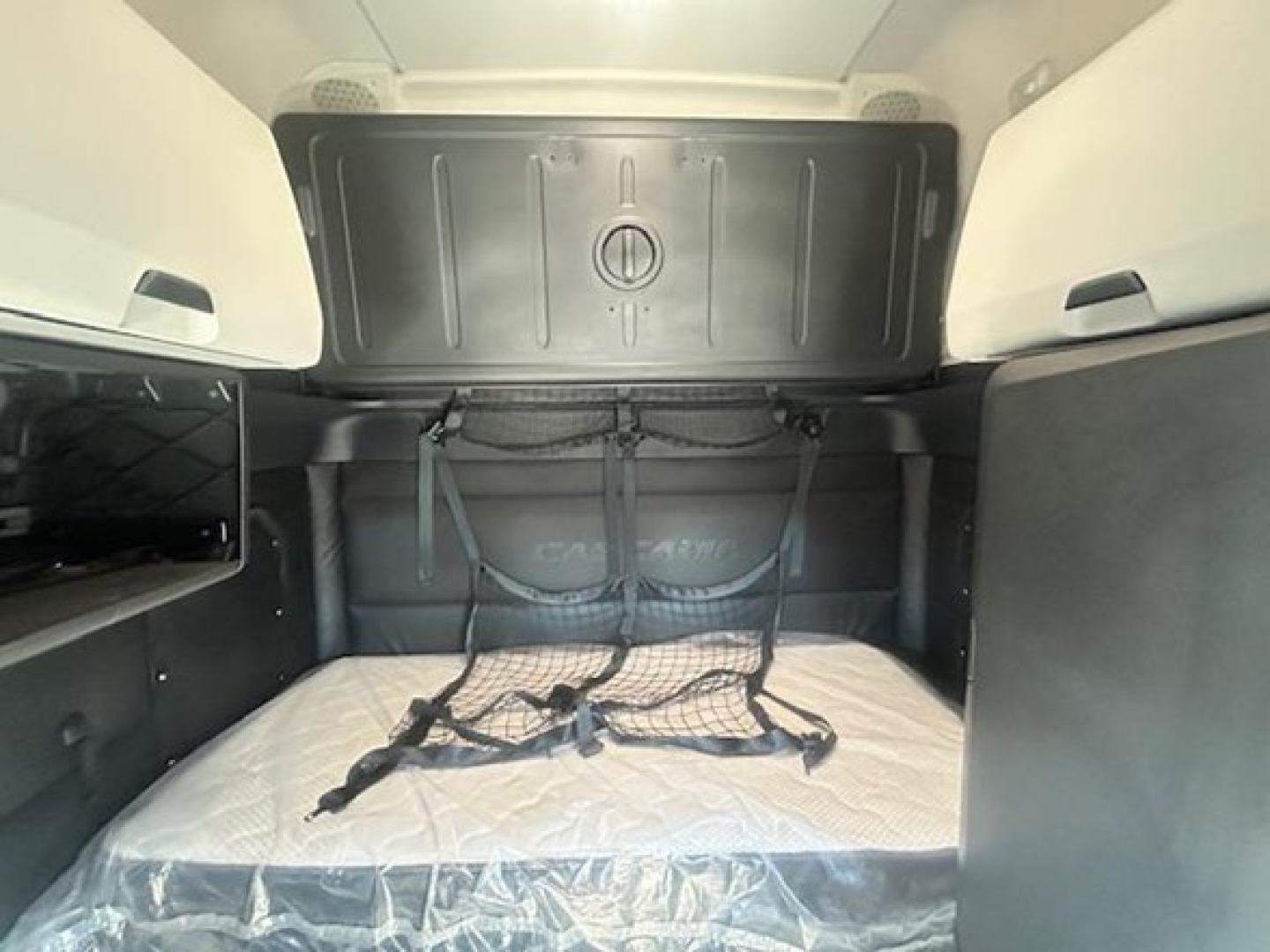 Tractor trailer sleeper cab interior showing bed with mattress, overhead storage bulkhead, and tie-down straps in a Freightliner Cascadia 126.