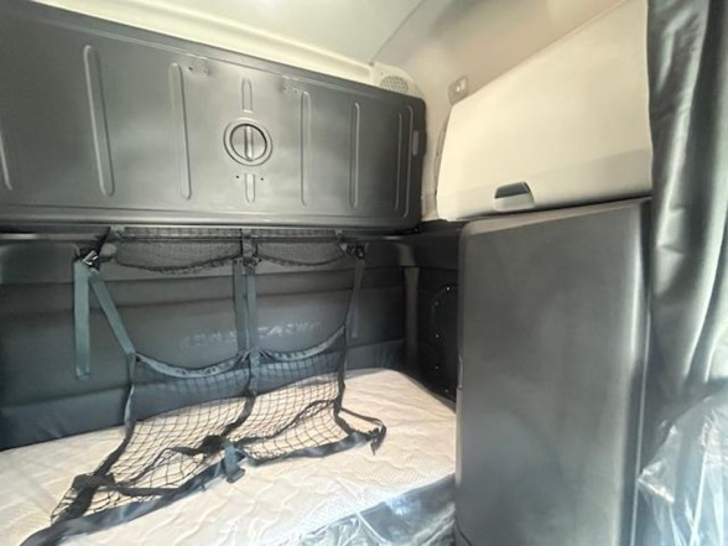 Tractor cab sleeper interior showing bunk bed area with netted storage and overhead storage panel