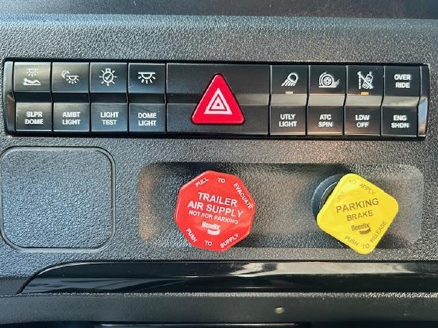 Truck dash panel showing warning lights and red emergency trailer supply cap and yellow parking brake cap.
