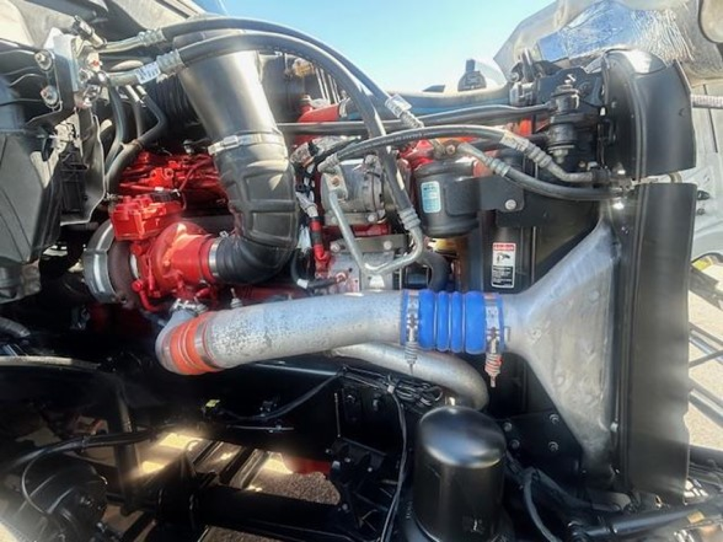 Truck engine bay showing turbocharger, hoses, radiator, and blue silicone hose clamp on a Freightliner Cascadia engine bay.
