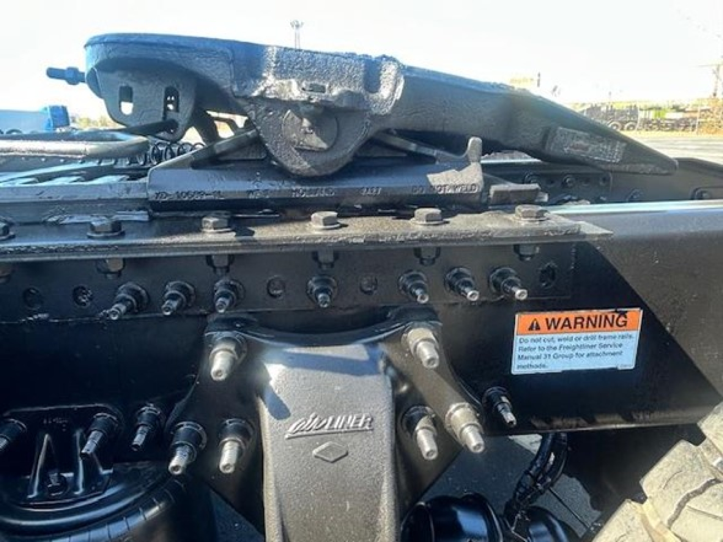 Conventional sleeper truck undercarriage view showing fifth wheel and mounting hardware with warning label and bolts.