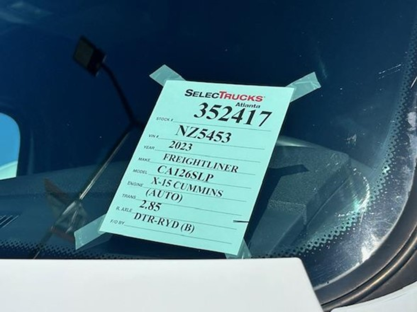 Vehicle sticker on windshield showing stock number 352417, year 2023 Freightliner Cascadia, model CA126GLP, engine N-15 Cummins, DTR-RYD(B) and other specs.