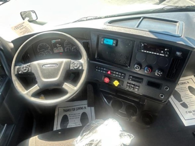 Cab interior of a Freightliner Cascadia 126 showing steering wheel, dashboard, and control panel with gauges and digital display.