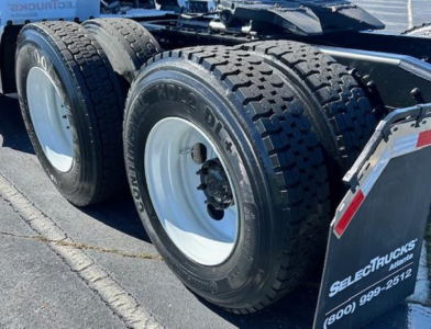 Triple axles truck rear wheels with heavy-duty tires and mud flaps showing Freightliner Cascadia 126 equipment labels.