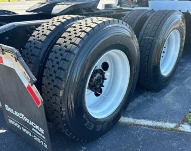 Freightliner Cascadia 126 rear dual wheels showing heavy tires and rear mud flaps with stock number and contact text.