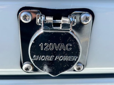 120V AC shore power inlet cover on Freightliner Cascadia 126, chrome with four screws and hinge.