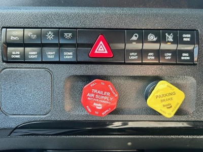 Truck dash panel showing warning lights and red emergency trailer supply cap and yellow parking brake cap.