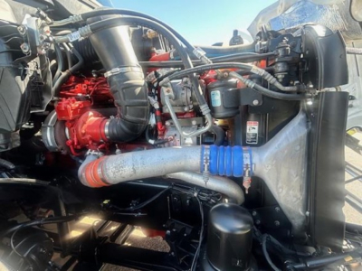 Truck engine bay showing turbocharger, hoses, radiator, and blue silicone hose clamp on a Freightliner Cascadia engine bay.