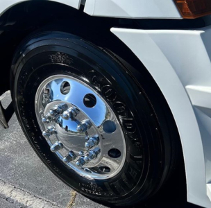 Front wheel and fender of a white Freightliner Cascadia 126 truck showing polished chrome hubcap and tire.