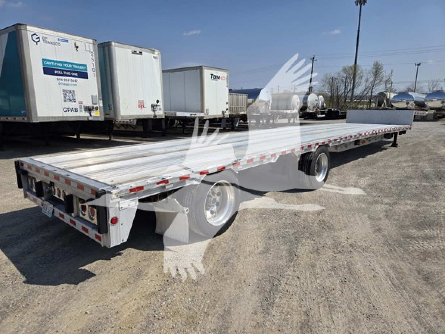 Flatbed trailer showing long aluminum deck with drop deck feature, rear lights, and dual rear axles in a used trailer lot.