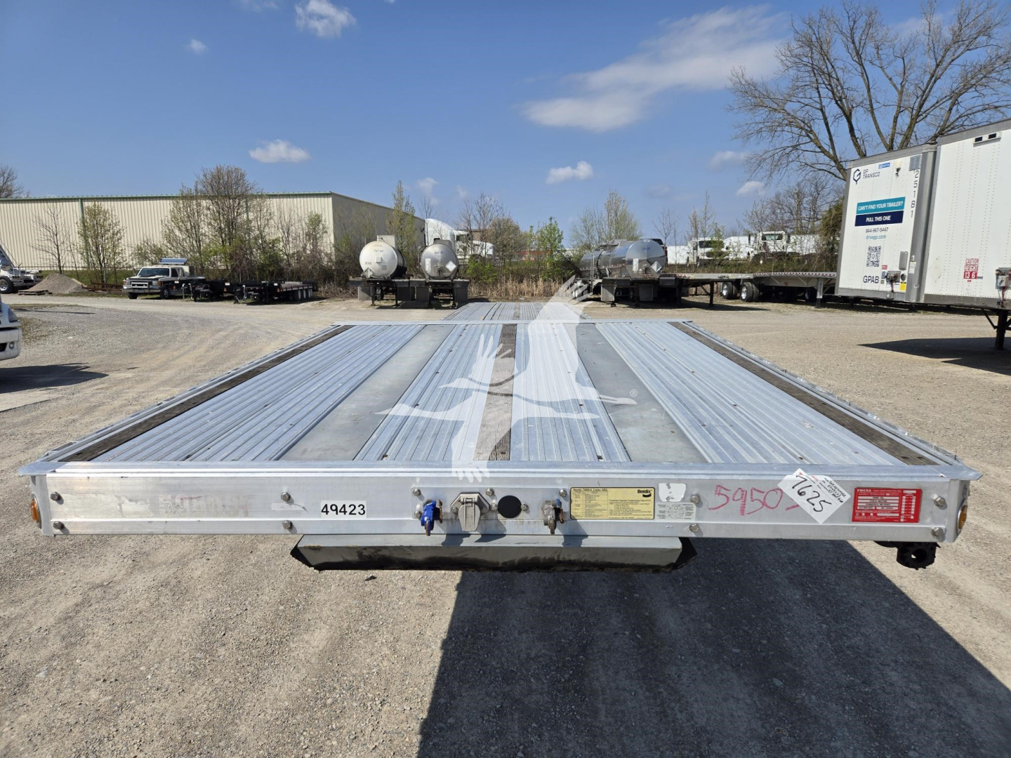 Drop deck trailer rear view showing metal deck plates and tail end with hitch and identification stickers.