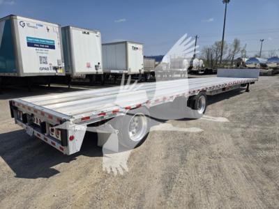 Flatbed trailer showing long aluminum deck with drop deck feature, rear lights, and dual rear axles in a used trailer lot.