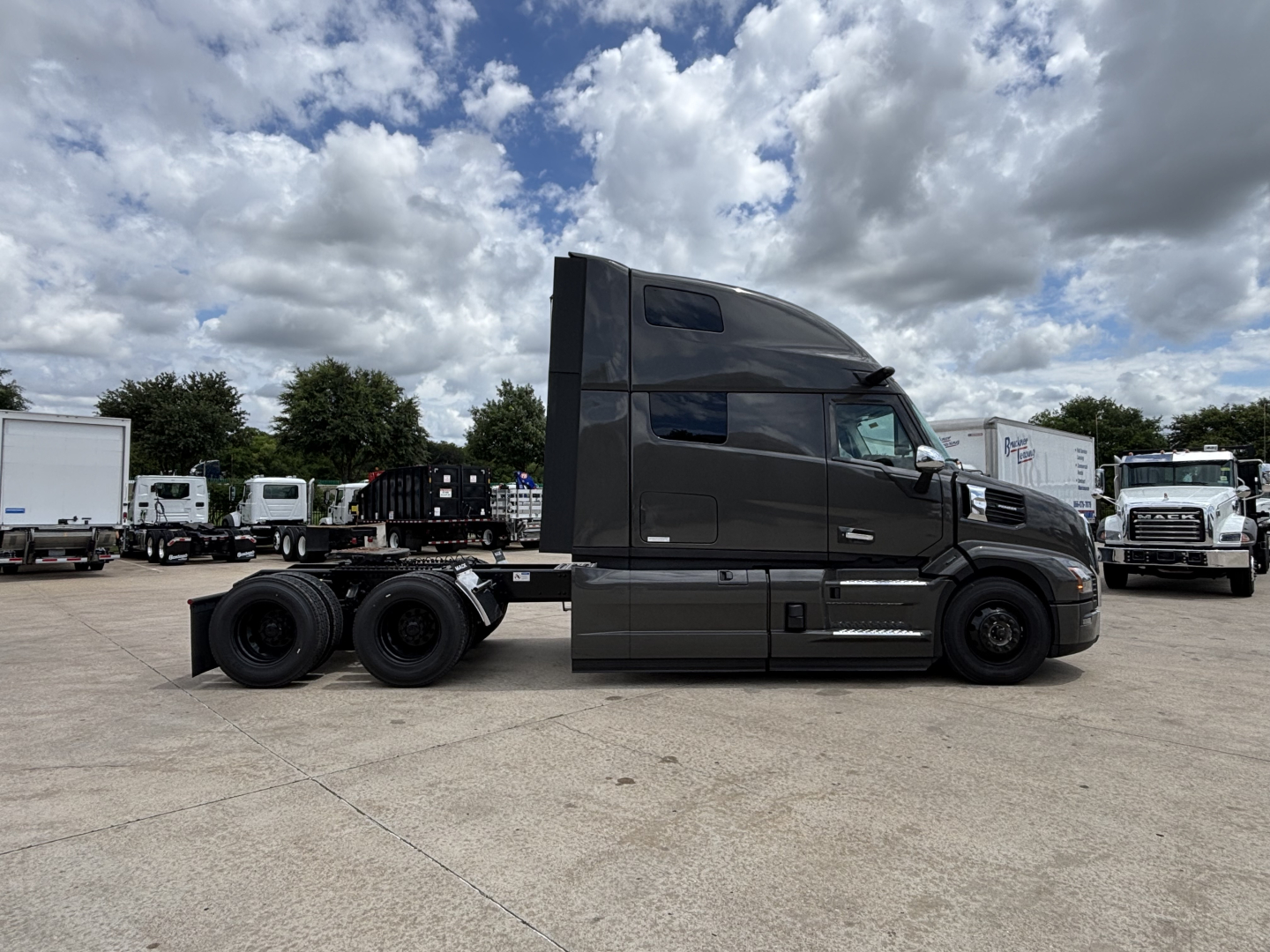 Side view of a 2027 Mack PR64T76H tractor in dark gray, showing the cab, fuel tanks, and dual rear axles. No visible text or labels legible on the truck.