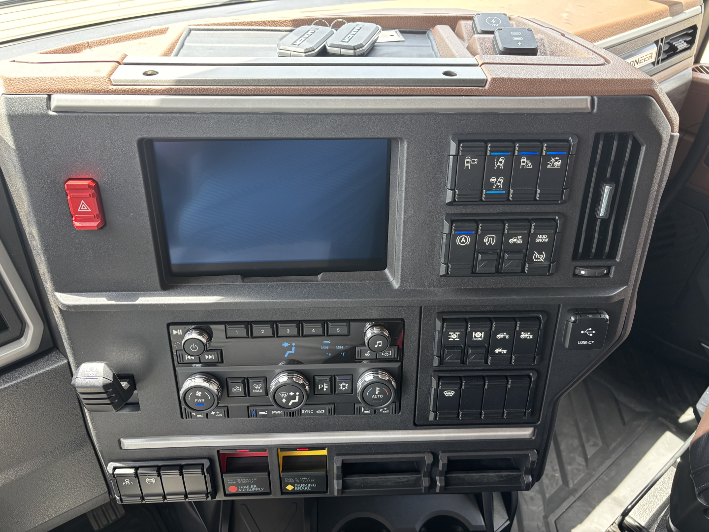 Truck cab front panel with large touchscreen display and control cluster; various switches and climate controls visible in dashboard view.