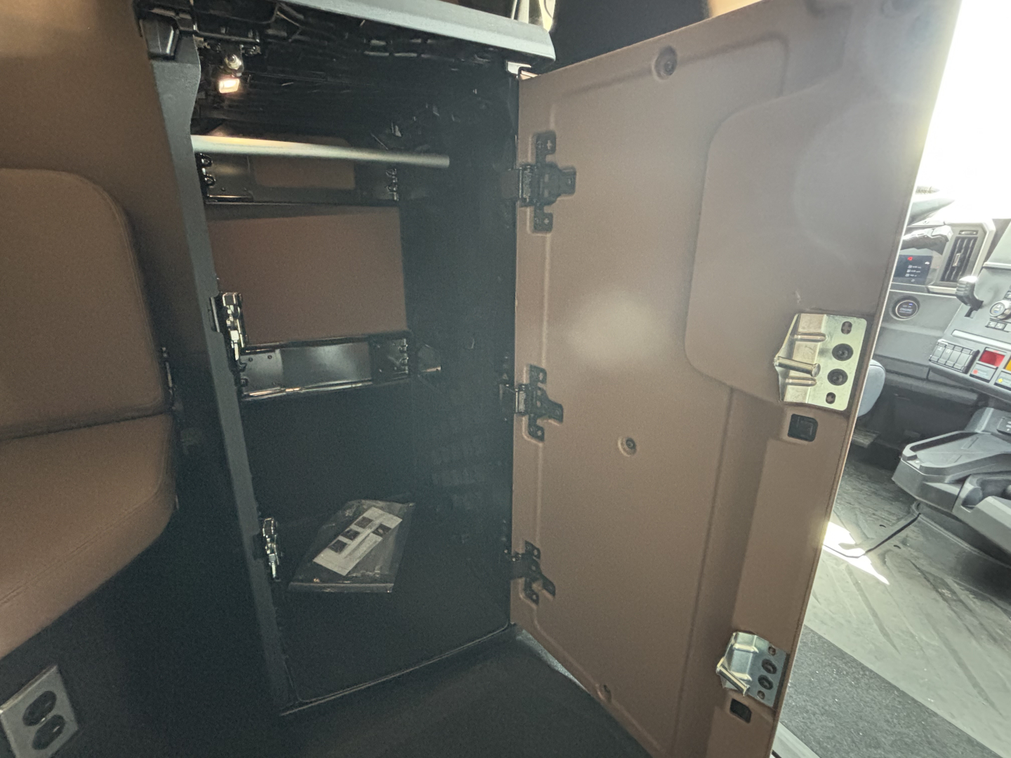 Cab interior of a new Mack PR64T76H showing an open storage cabinet with shelves and a small box inside.