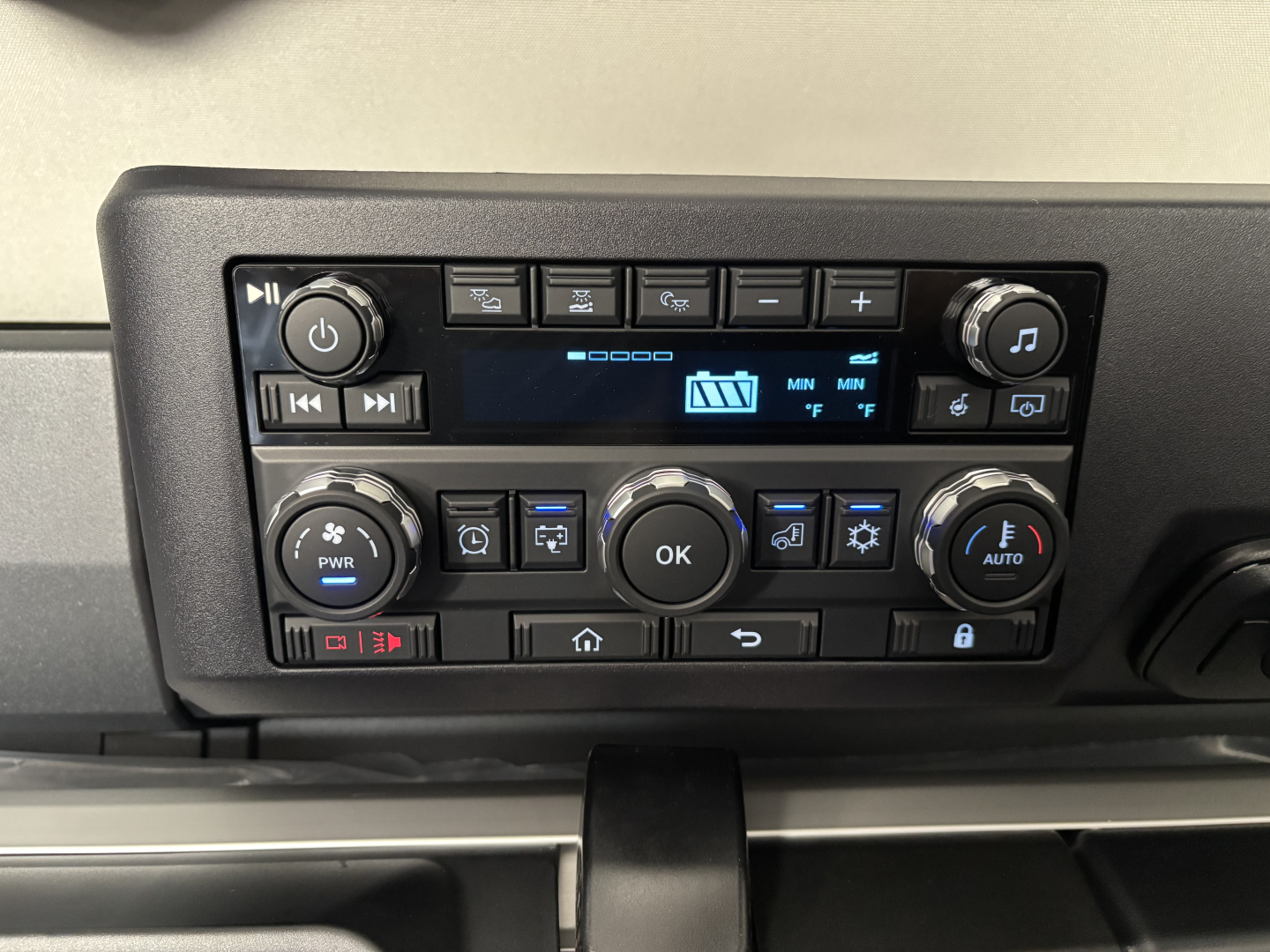 Truck dashboard panel with climate controls and media buttons; no legible brand text visible.