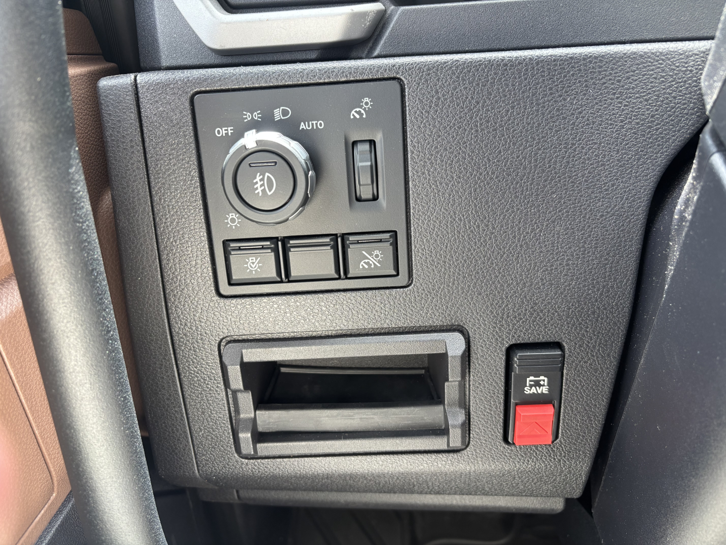 Dashboard controls of a 2027 Mack PR64T76H showing headlight switch, fog light icon, and window/seat switch panel near a recessed cubby; red engine kill switch labeled 'FIRE' not present; small storage slot.