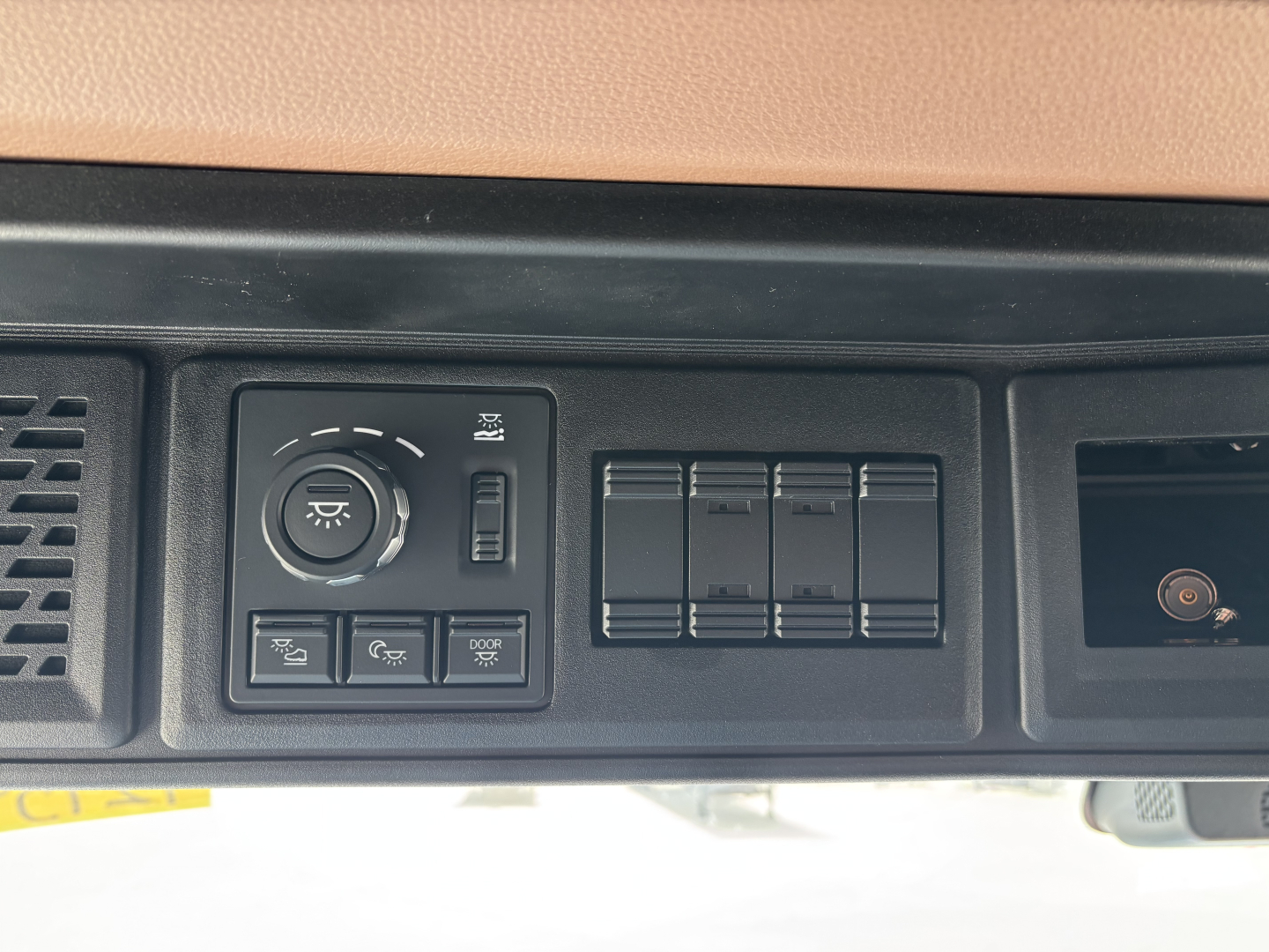 Dashboard controls of a Mack truck showing a circular dial, four rectangular switches, and a series of blank rocker panels.