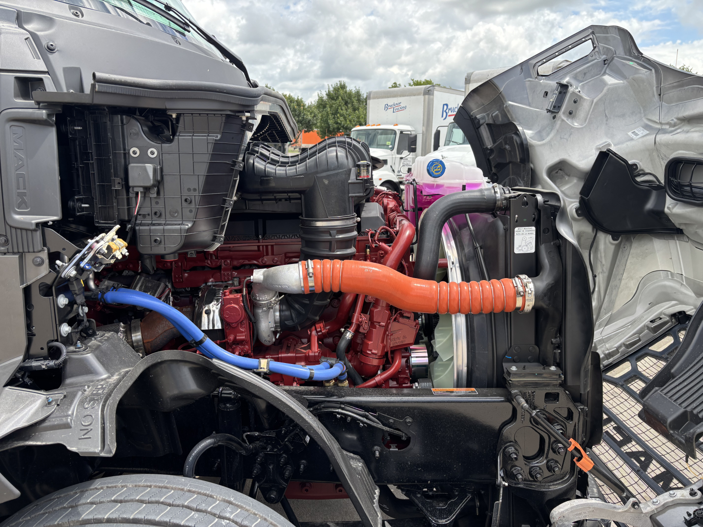 Mack PR64T76H engine bay with orange high-temperature coolant hose, blue hose, and red engine block visible between open cab sections.