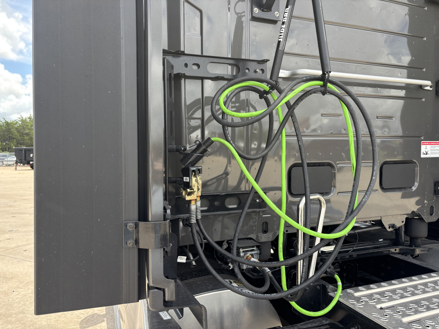 Mack PR64T76H truck rear view showing hydraulic lines and electrical cables with green and black sheathing near side step and rear panel.