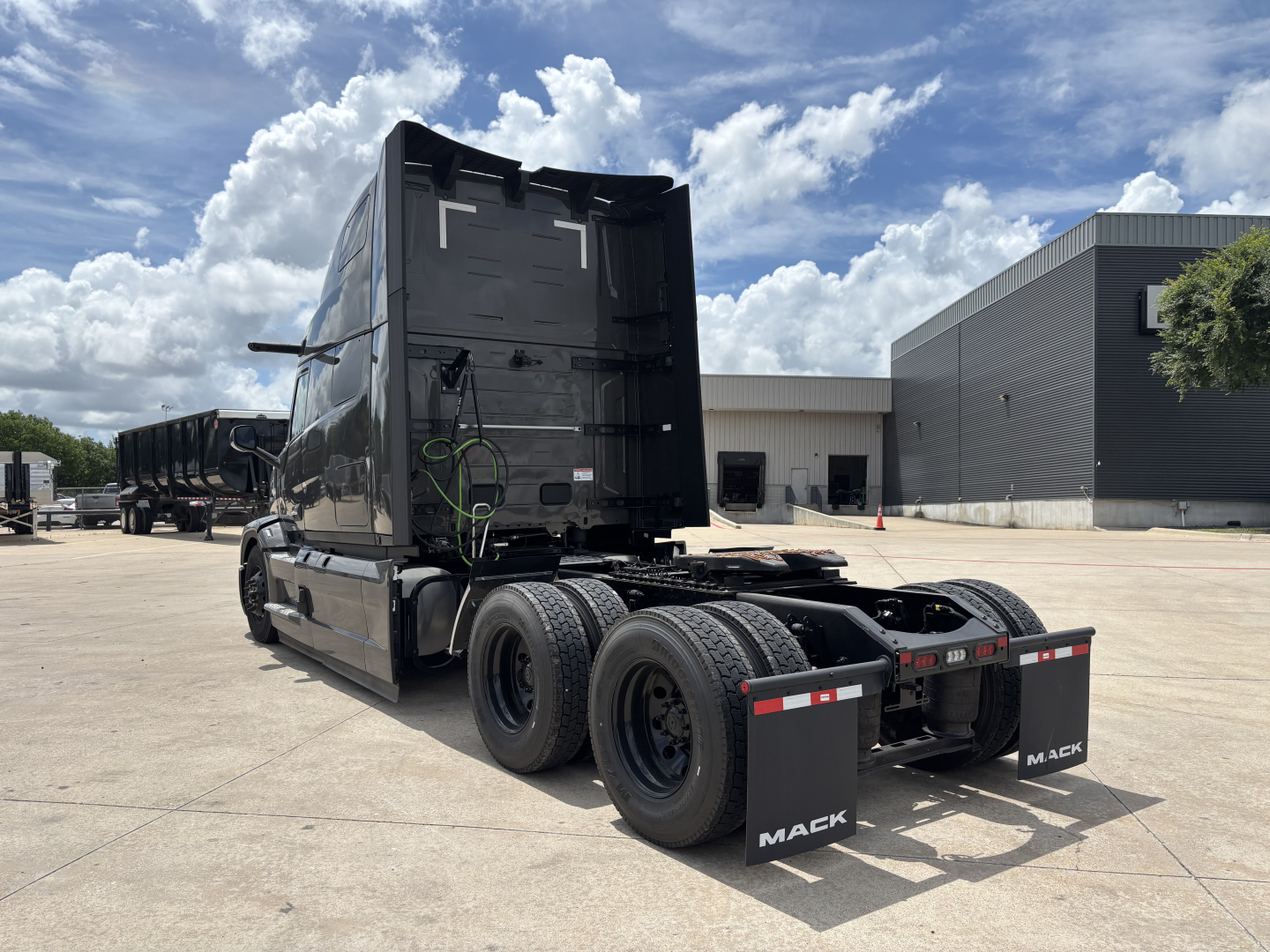 Mack PR64T76H conventional sleeper truck viewed from rear-left, showing dual rear axles, mudflaps with Mack branding, and bare chassis in parking lot.