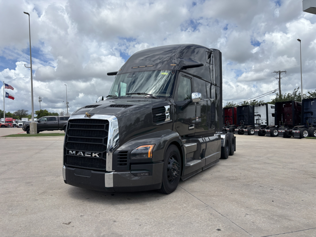 Mack PR64T76H conventional sleeper truck in a dealership lot, dark gray with chrome grille and steps.