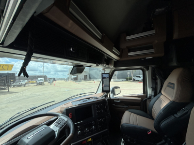 Truck cab interior of a 2027 Mack PR64T76H showing dashboard and passenger seat with overhead storage compartments and windows.
