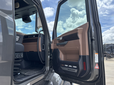 Truck cab interior shows open driver door with brown and black interior panels, Mack badge on door sill, dashboard and steering wheel visible.