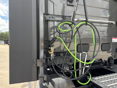 Mack PR64T76H truck rear view showing hydraulic lines and electrical cables with green and black sheathing near side step and rear panel.
