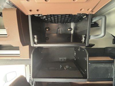Cab interior showing two open overhead compartments in a Mack PR64T76H truck, with visible mounting brackets and wiring inside the lower dash compartment.