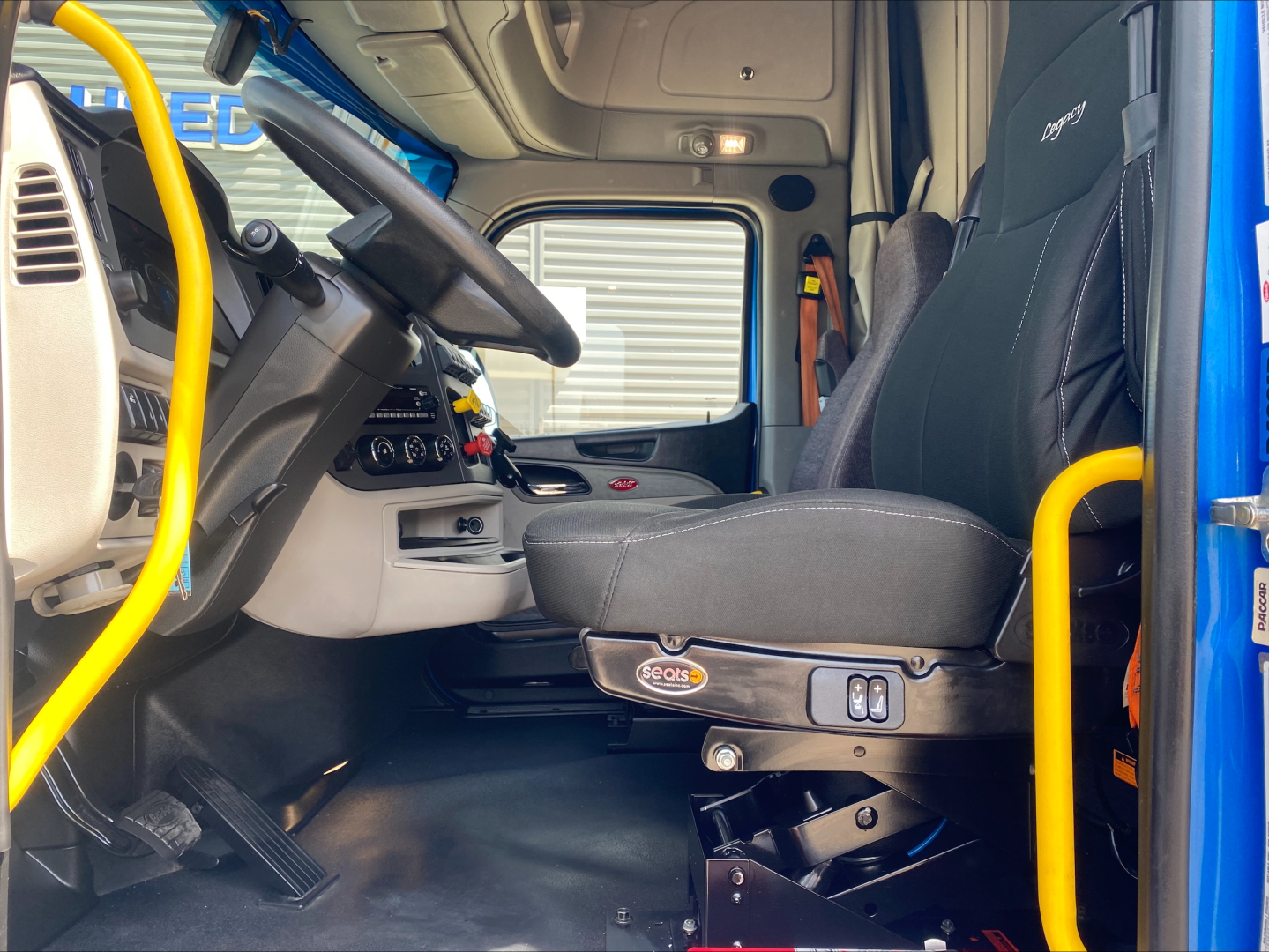 Cab interior of a 2022 Peterbilt 579 truck showing driver seat, steering wheel, dashboard, and yellow grab handles.