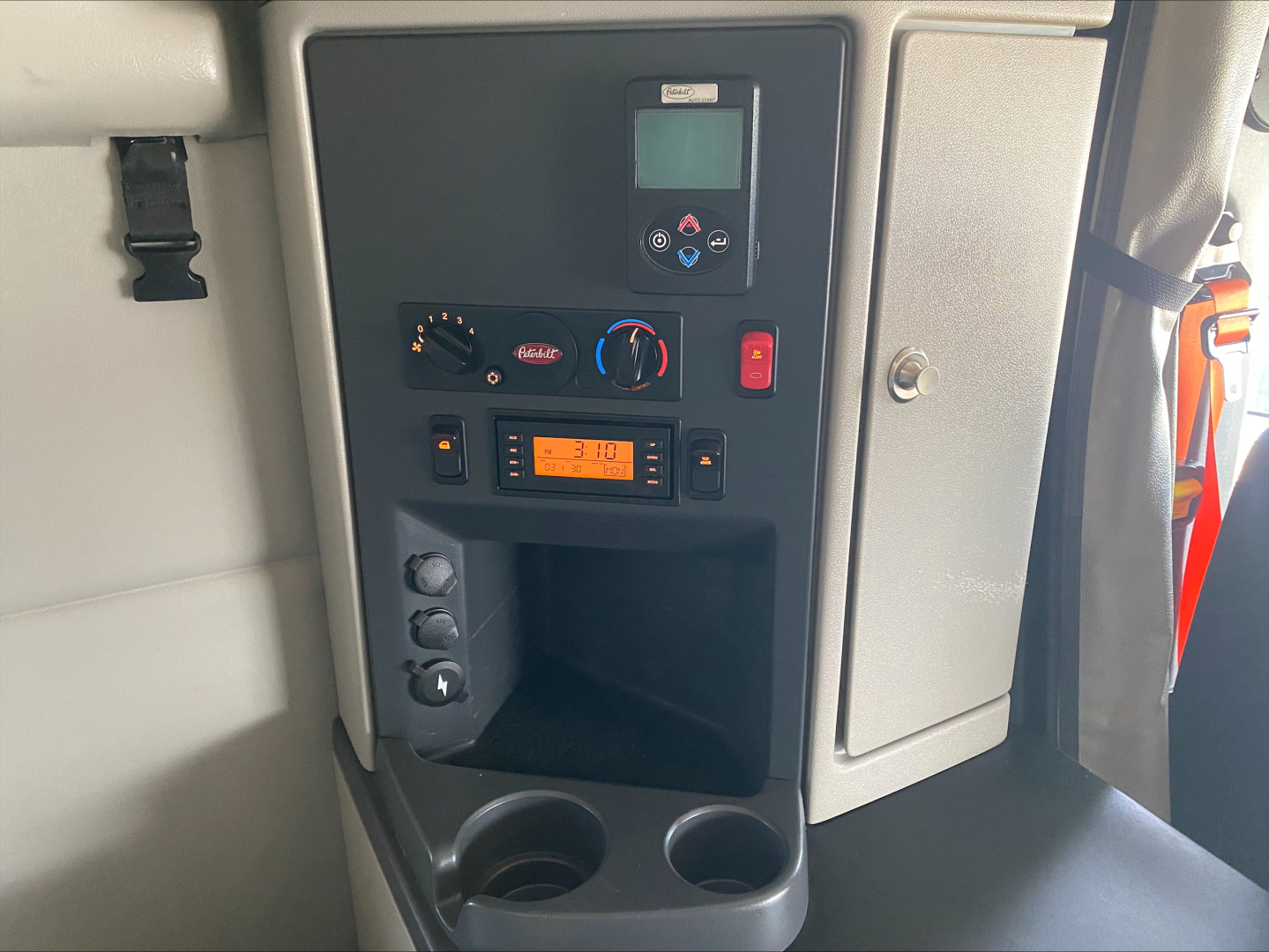 Truck cab dashboard/console showing control panel with digital display, knobs, and switches; cup holders at bottom.