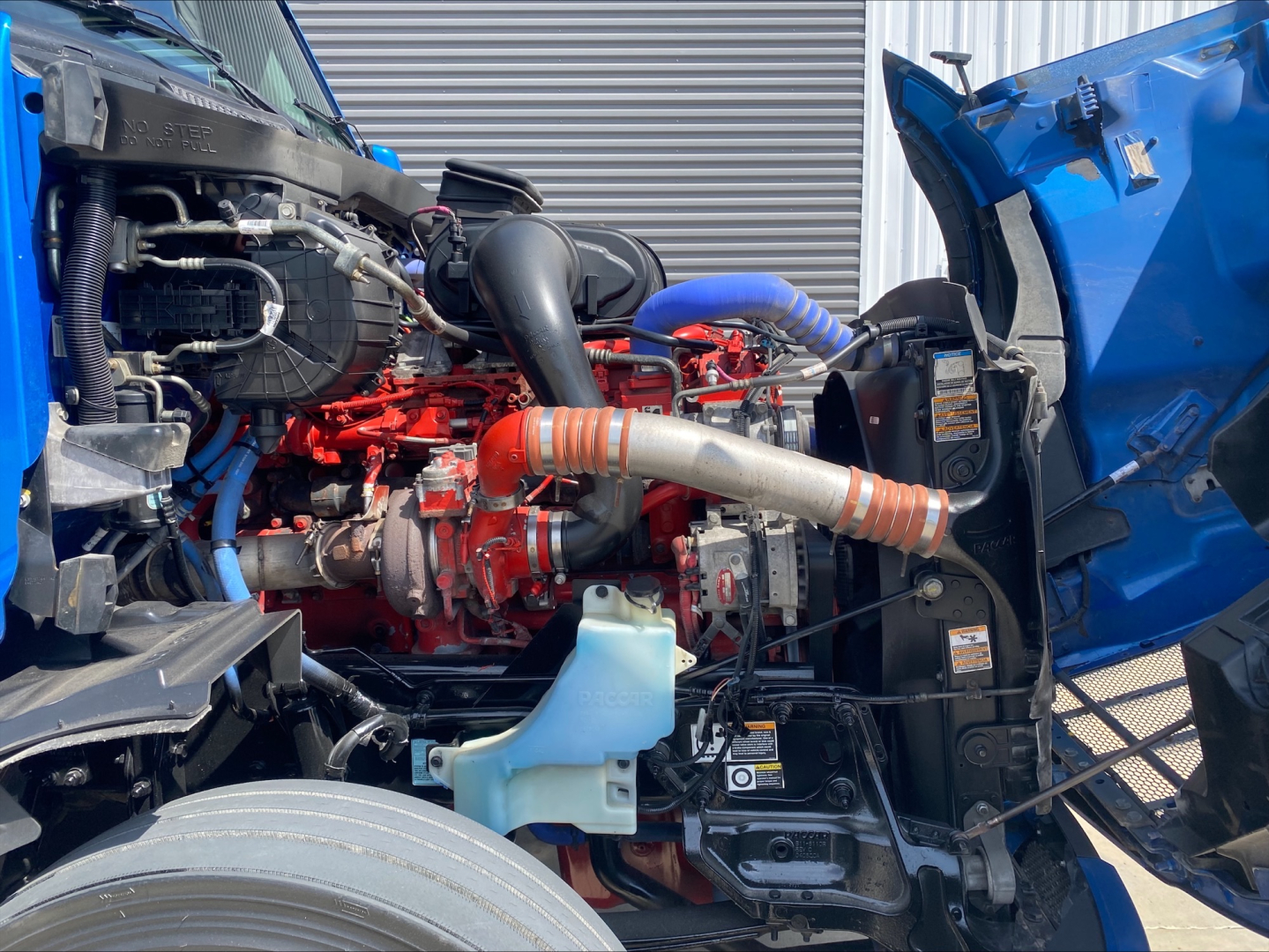 peterbilt 579 engine bay showing diesel engine with red and blue hoses, intake, coolant reservoir, and open hood