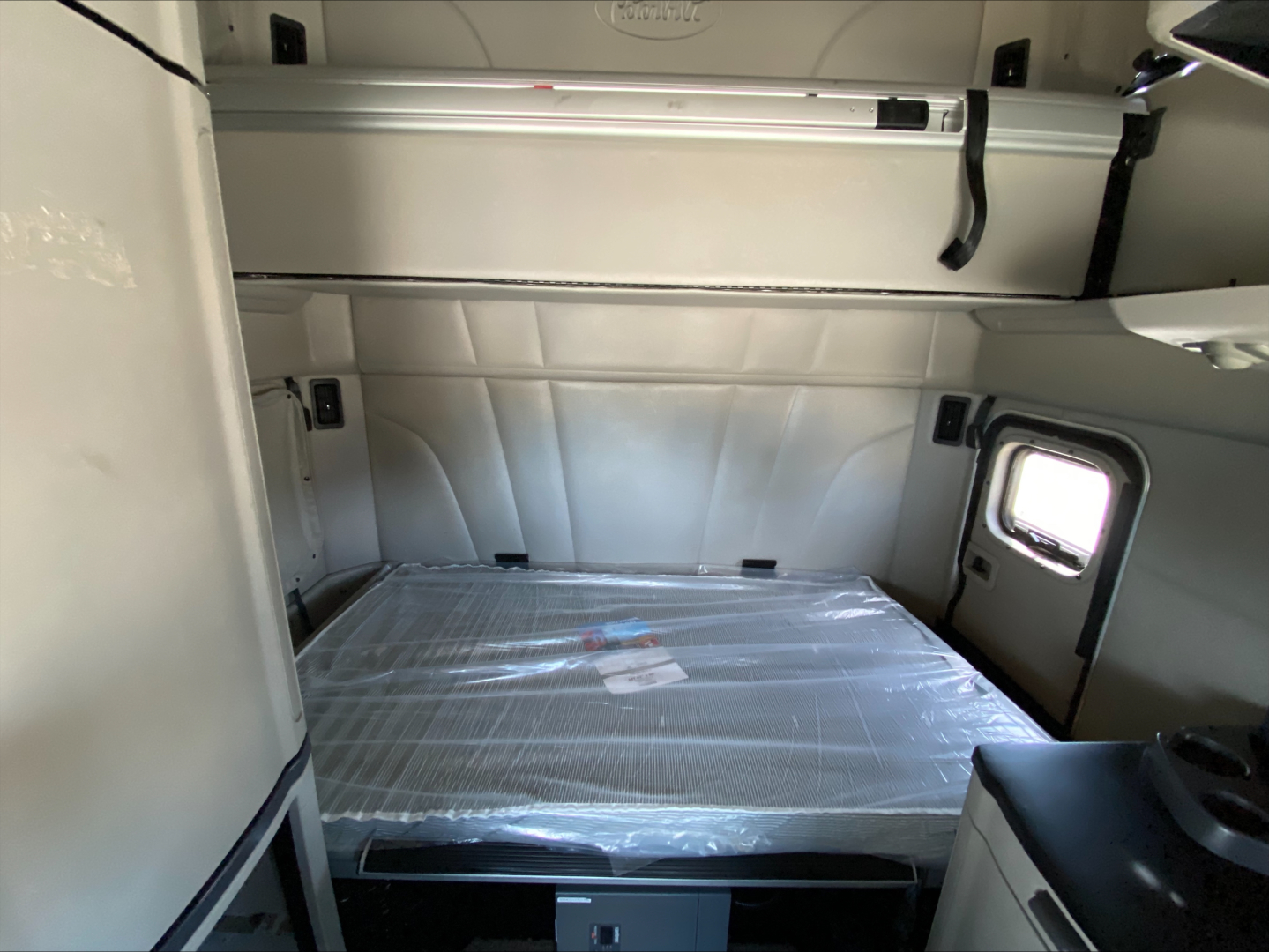 Cab sleeper area of a 2022 Peterbilt 579 truck showing bunk bed with plastic cover and storage compartments.