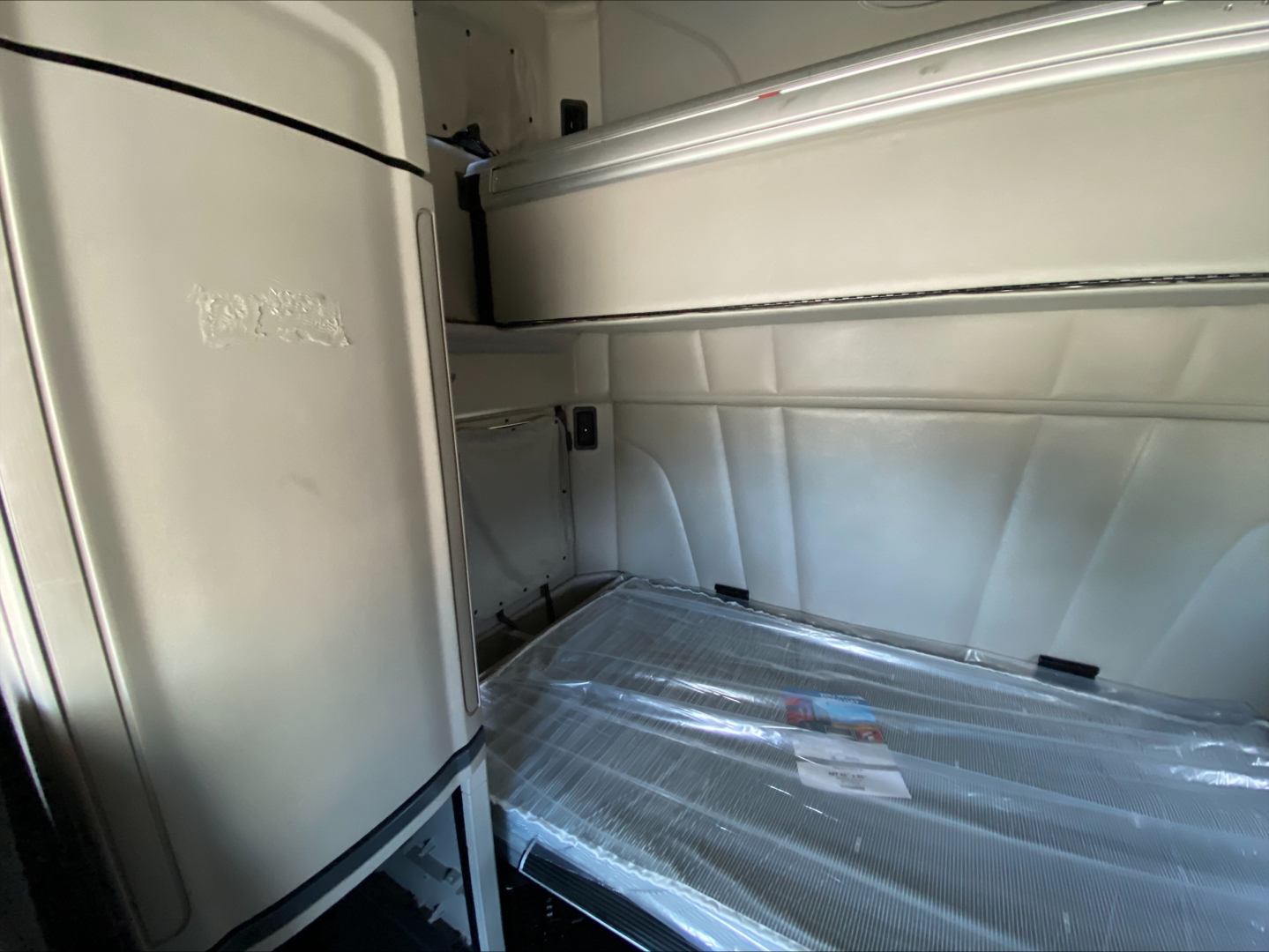 Peterbilt 579 truck sleeper cab interior cargo area with plastic-wrapped floor and storage compartment wall