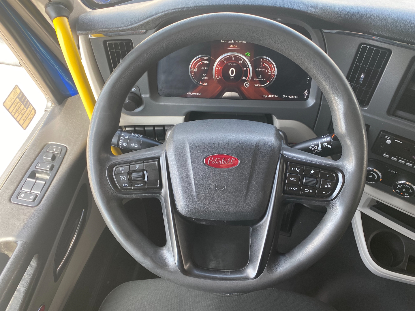 Peterbilt 579 truck cockpit steering wheel with digital instrument cluster and controls on both sides, driver door panel visible