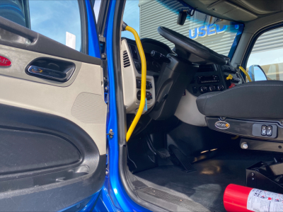 Truck cab interior of a blue 2022 Peterbilt 579 showing steering wheel, dashboard, and driver seat area.