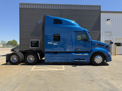 Peterbilt 579 tractor in blue, side view showing sleeper cab, three rear axles, chrome wheels, and fuel tanks.