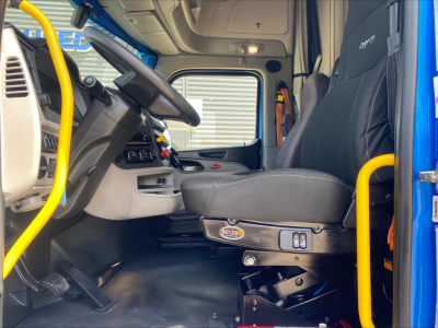 Cab interior of a 2022 Peterbilt 579 truck showing driver seat, steering wheel, dashboard, and yellow grab handles.