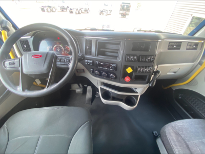 Truck cabin interior of a 2022 Peterbilt 579 showing steering wheel with Peterbilt logo, dashboard with gauges, center console, climate controls, and cup holders.