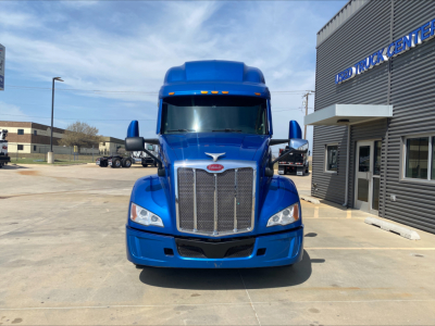 Blue 2022 Peterbilt 579 conventional sleeper truck front view with chrome grille and Peterbilt badge, in a dealership lot.
