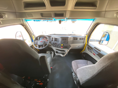 Peterbilt 579 interior cab layout seen from back seat showing steering wheel, instrument cluster, center console, and grey fabric seats.