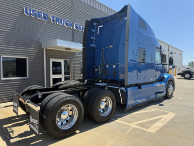 Peterbilt 579 tractor in blue, side view showing sleeper cab, chassis, dual rear axles, and showroom building in background with 'USED TRUCK CENTER' signage.